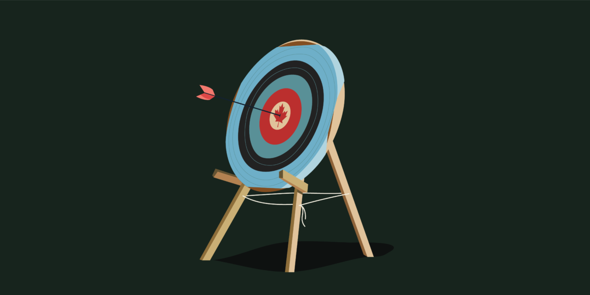 An archery board with an arrow hitting the bullseye which is a maple leaf meant to look like a Canadian flag. There is one red ring around, a teal one, a navy one, and a light blue one on the outside. It has all been placed on a wooden stand.